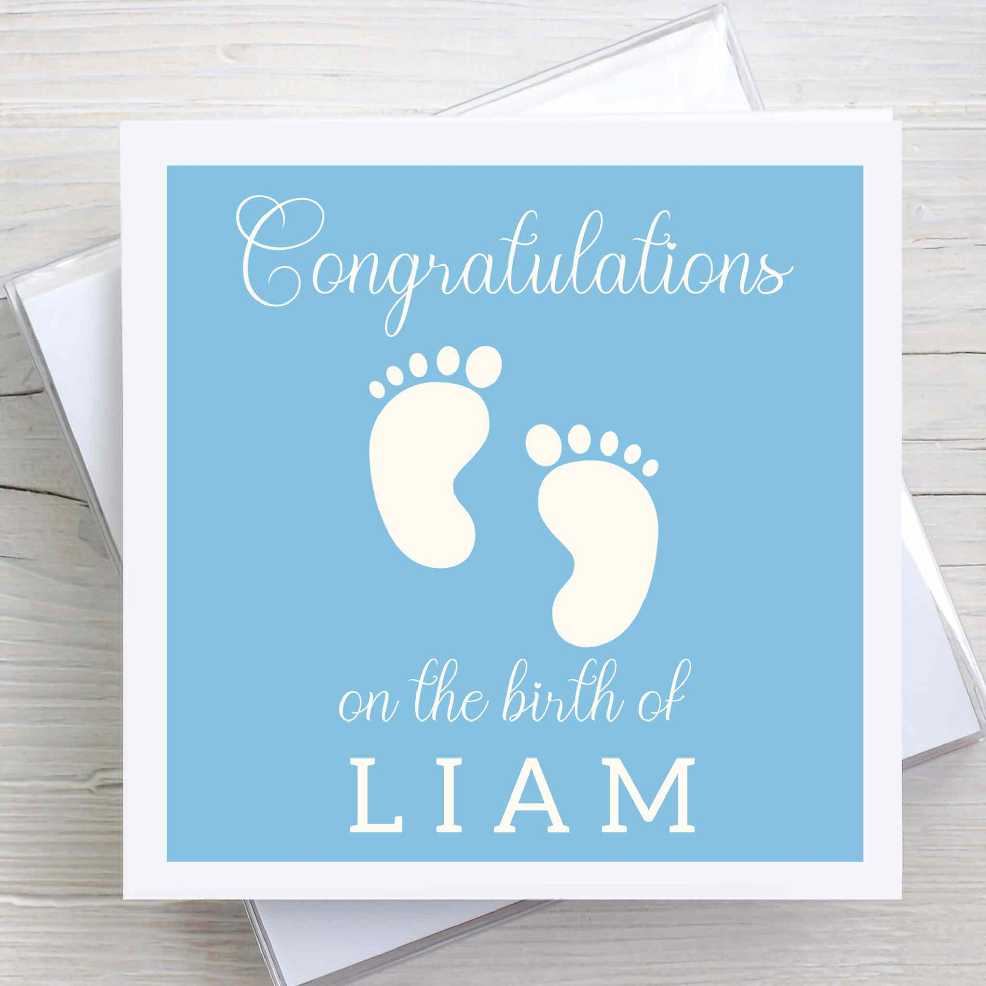 New baby congratulations card featuring baby feet design. Baby name on front. Blue coloured background.